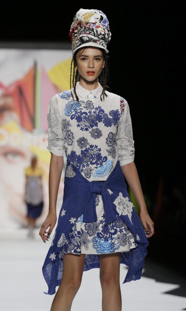 Ein Model mit einem Hut aus Stoffresten präsentiert ein blau-weißes Kleid mit Blumenmuster.