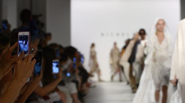 Zuschauer fotografieren Models auf dem Laufsteg einer Modenschau.