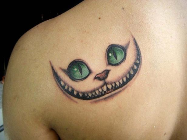 Ein Tattoo auf einer Schulter zeigt das Grinsen der Grinsekatze aus Alice im Wunderland.