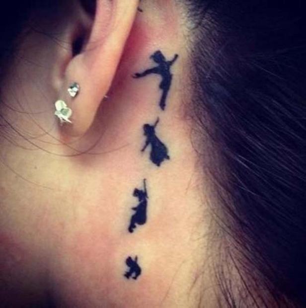 Ein Tattoo mit den Silhouetten von Peter Pan und den verlorenen Kindern hinter dem Ohr einer Person.