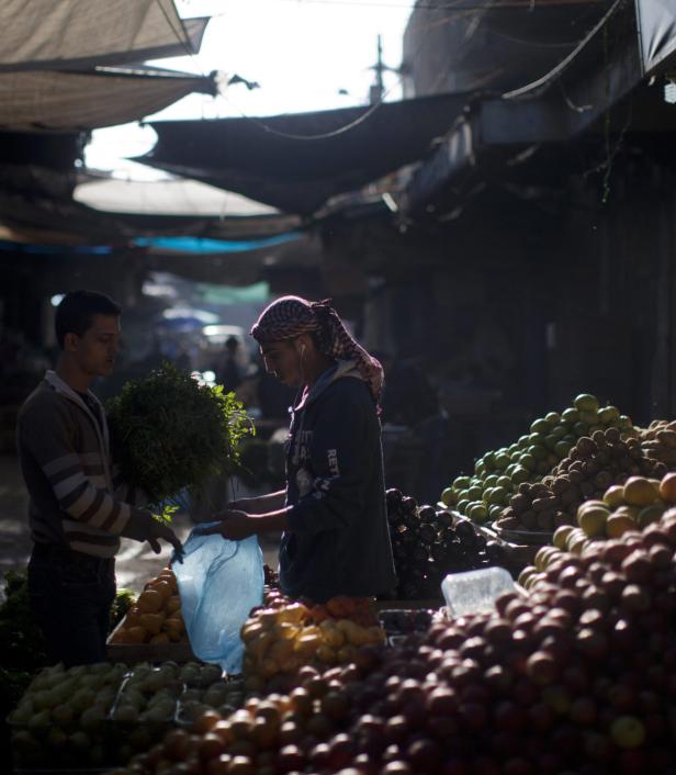 Auf einem Markt kauft ein Mann mit Kopfbedeckung Kräuter von einem Verkäufer.