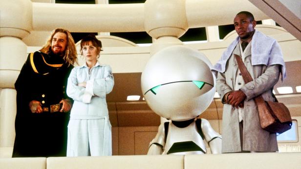 Vier Charaktere, darunter ein Roboter, stehen in einer hellen, futuristischen Umgebung.