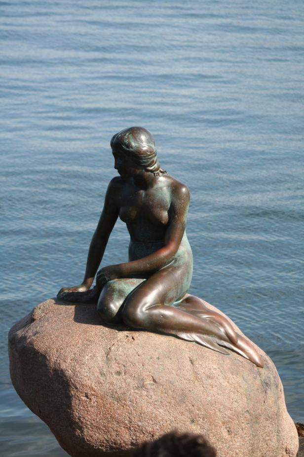Die Statue der kleinen Meerjungfrau sitzt auf einem Felsen am Wasser.