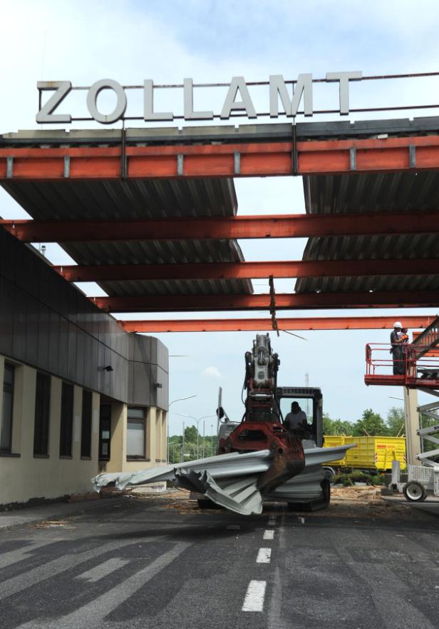 Ein Bagger demontiert das Schild „Zollamt“ an einem Grenzübergang.
