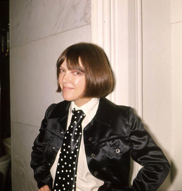 Eine Frau mit dunklen Haaren, gekleidet in eine schwarze Jacke und eine gepunktete Krawatte.