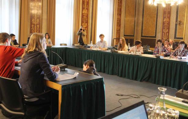 Personen sitzen an einem U-förmigen Tisch in einem Konferenzraum.