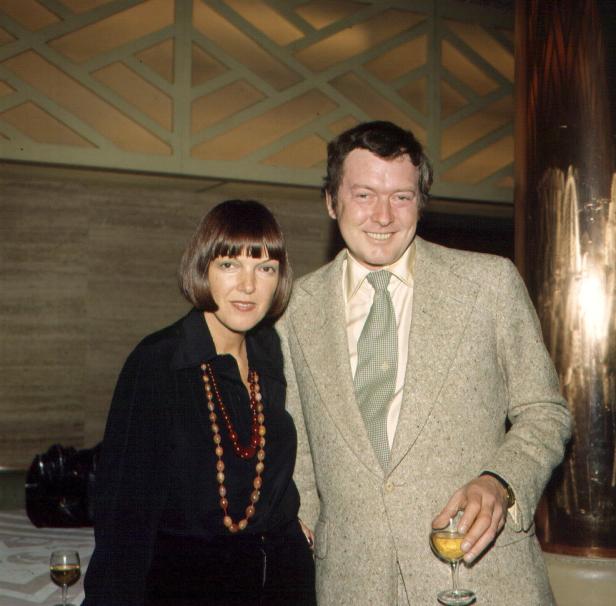 Eine Frau mit dunklem Haar und ein Mann mit einem Glas Wein posieren für ein Foto.
