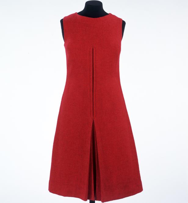 Ein ärmelloses, rotes Kleid mit einer Falte in der Mitte hängt an einer Schneiderpuppe.