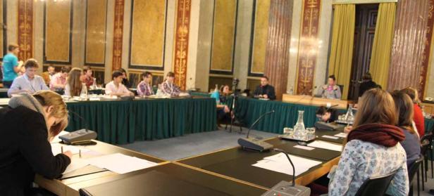 In einem Konferenzraum sitzen Menschen an Tischen und nehmen an einer Sitzung teil.