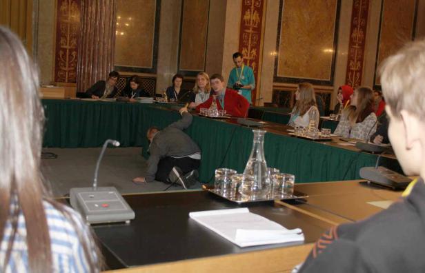 Ein Mann kriecht auf dem Boden vor einer Gruppe von Menschen an einem Tisch.