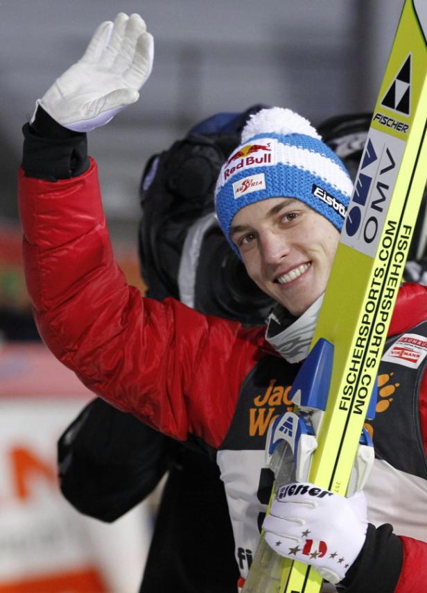 Ein Skispringer mit Mütze und Skiern winkt in die Kamera.