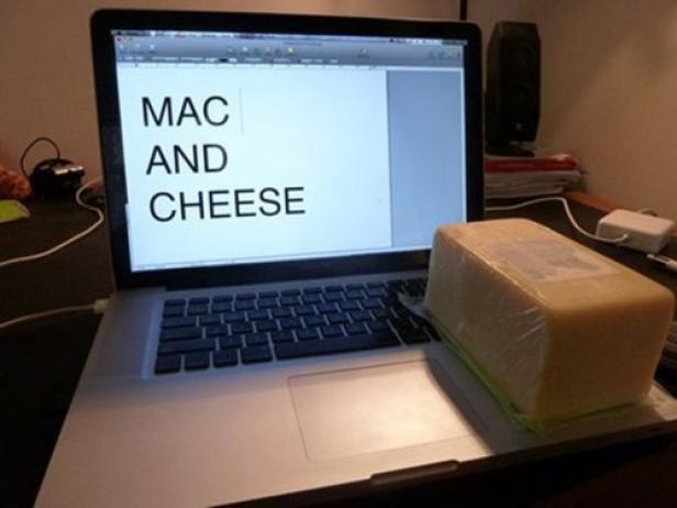 Ein Laptop zeigt den Text „Mac and Cheese“, während ein großer Käseblock auf der Tastatur liegt.