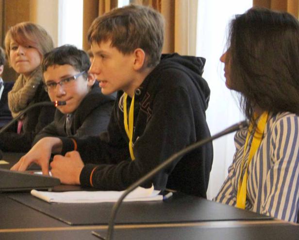 Jugendliche sitzen an einem Tisch mit Mikrofonen und diskutieren.