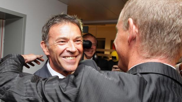 Ein lächelnder Mann wird von Reportern interviewt.