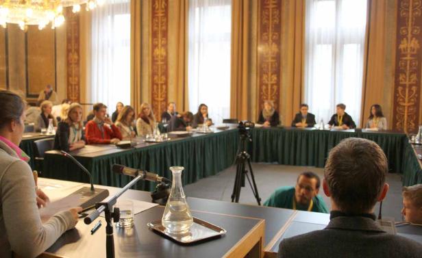 Menschen sitzen an einem U-förmigen Tisch in einem Konferenzraum.