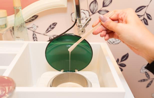 Eine Hand hält einen Spatel mit Wachs über einen Wachswärmer.