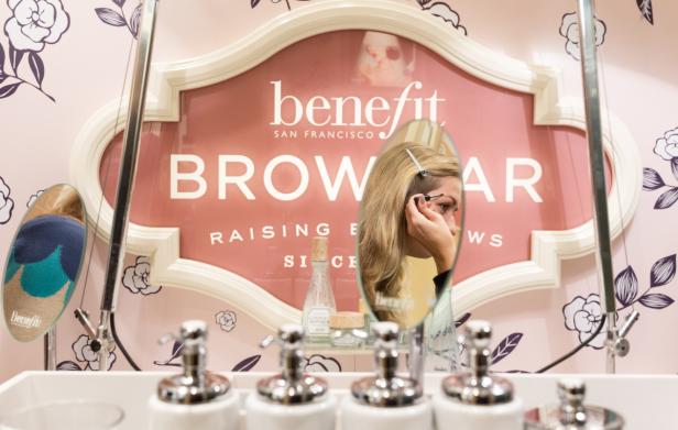 Eine Frau zupft ihre Augenbrauen vor einem Spiegel in einer Benefit Brow Bar.