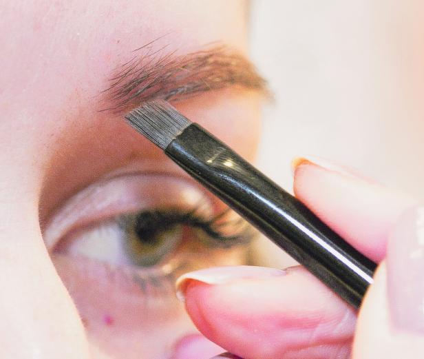 Eine Person trägt mit einem Pinsel Make-up auf ihre Augenbrauen auf.