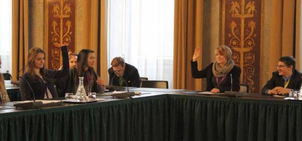 Mehrere Personen sitzen an einem Tisch und heben ihre Hände.