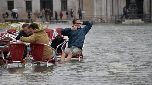 Männer sitzen im Hochwasser auf Stühlen in Venedig.