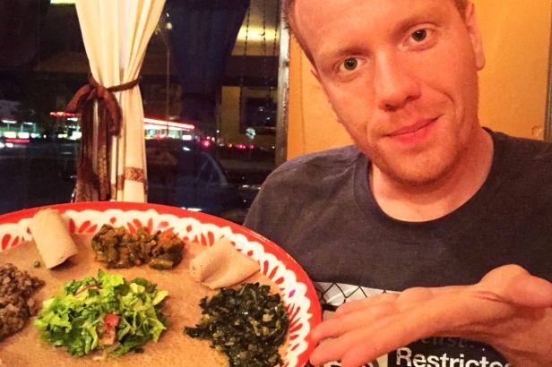 Ein Mann präsentiert ein Gericht der äthiopischen Küche mit Injera-Brot und verschiedenen Beilagen.