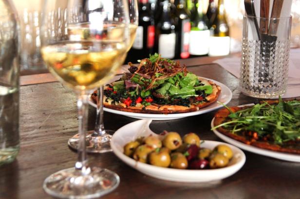 Ein Tisch mit Pizza, Oliven und Gläsern mit Weißwein.