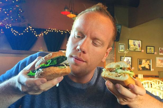 Ein Mann hält zwei Hälften eines belegten Brötchens in seinen Händen.