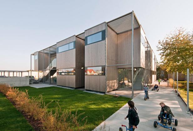 Kinder spielen vor einem modernen Gebäude mit Holzfassade.