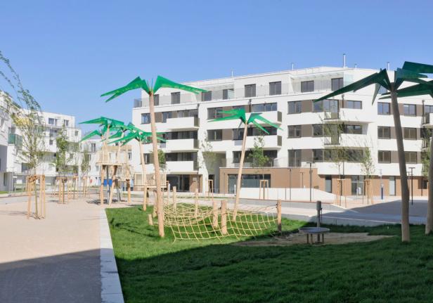 Ein Spielplatz mit künstlichen Palmen vor modernen Wohnhäusern.