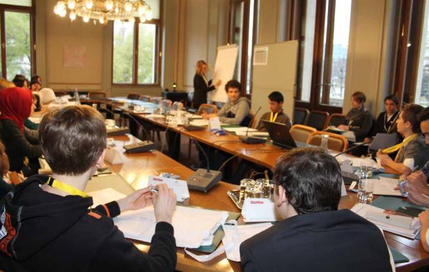 Teilnehmer sitzen an einem langen Tisch während einer Präsentation.