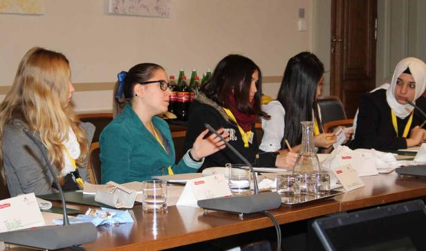 Fünf junge Frauen sitzen an einem Tisch bei einer Konferenz oder einem Meeting.