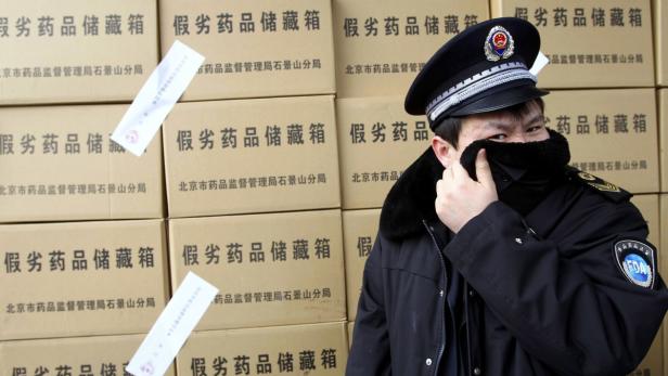 Ein chinesischer Beamter steht vor Kisten mit der Aufschrift „gefälschte Medikamente“.