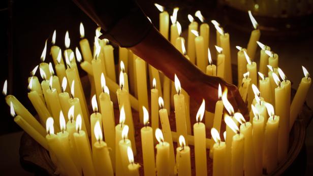 Eine Hand inmitten vieler brennender Kerzen.