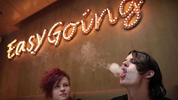 Ein Mann raucht eine E-Zigarette unter einem Leuchtschild mit der Aufschrift „Easy Going“.