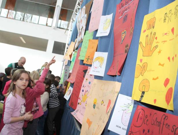 Eine Gruppe von Kindern betrachtet eine Wand mit bunten, selbstgemalten Bildern.
