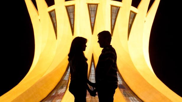 Ein Paar steht Händchen haltend vor der Kathedrale von Brasília.