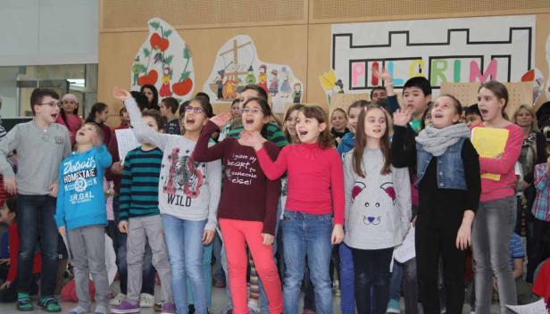 Eine Gruppe von Kindern singt vor einer Wand mit dem Wort „Pilgrim“.