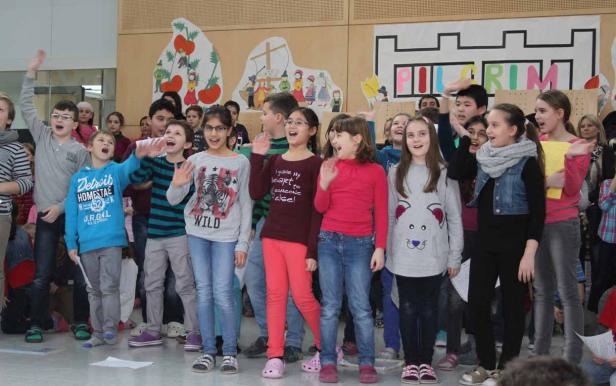 Eine Gruppe von Kindern singt auf einer Bühne vor einem Wandbild.