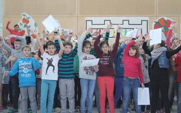 Eine Gruppe von Kindern steht auf einer Bühne und singt mit erhobenen Händen.