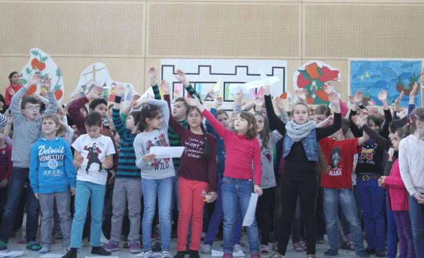 Eine Gruppe von Kindern steht mit erhobenen Händen vor Wandbildern.