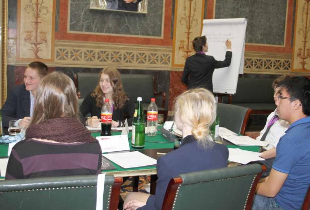 Eine Gruppe von Menschen sitzt an einem Tisch, während eine Person an einem Flipchart schreibt.