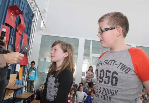 Zwei Kinder stehen vor einer Gruppe von Zuschauern und einem Mikrofon.