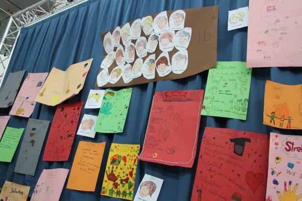 An einer blauen Wand hängen viele bunte Kinderzeichnungen.