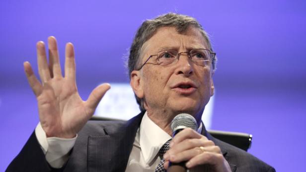 Bill Gates spricht bei einer Veranstaltung und hebt seine Hand.