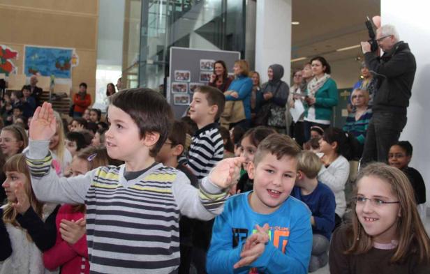 Eine Gruppe von Kindern klatscht und winkt in einem großen Raum.