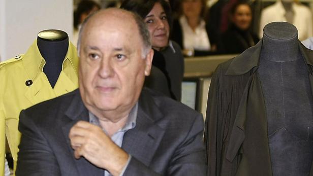 Amancio Ortega, Gründer von Zara, posiert zwischen zwei Schaufensterpuppen mit Mänteln.