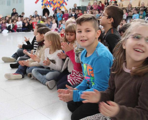 Eine Gruppe von Kindern sitzt auf dem Boden und klatscht in die Hände.