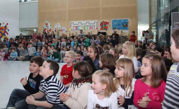 Eine große Gruppe von Kindern sitzt auf dem Boden und schaut aufmerksam zu.