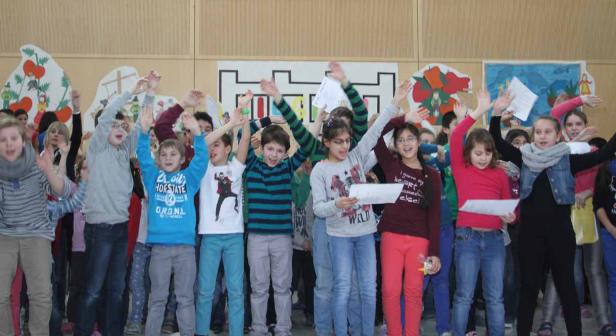 Eine Gruppe von Kindern steht auf einer Bühne und singt mit erhobenen Händen.