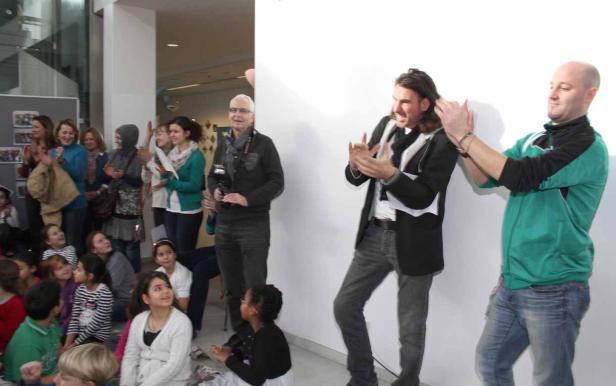 Zwei Männer führen vor einer Gruppe von Kindern und Erwachsenen eine Performance auf.